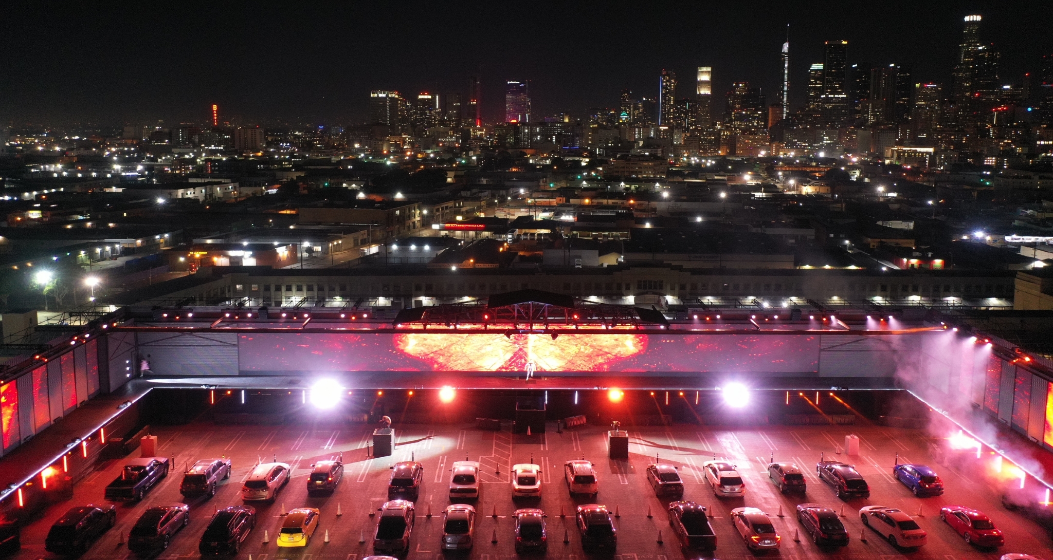Cars lined up in front of massive screens on top of a parking structure with Downtown Los Angeles as a backdrop.